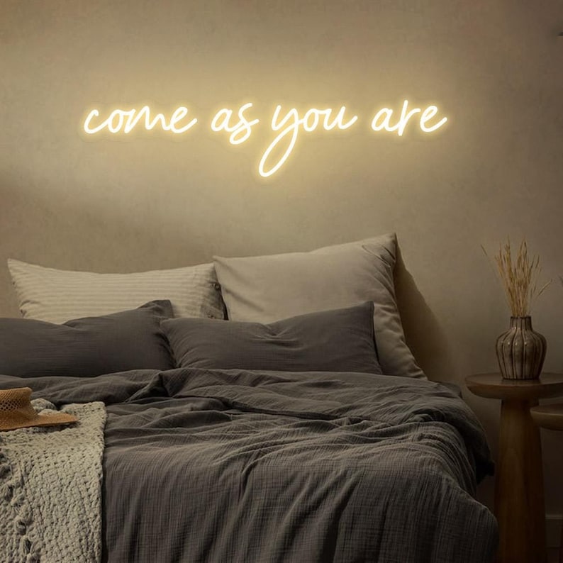Come As You Are" LED Neon sign by by LedNeons.com - creating a fun and inspiring atmosphere. - glowing warmly on a wall.