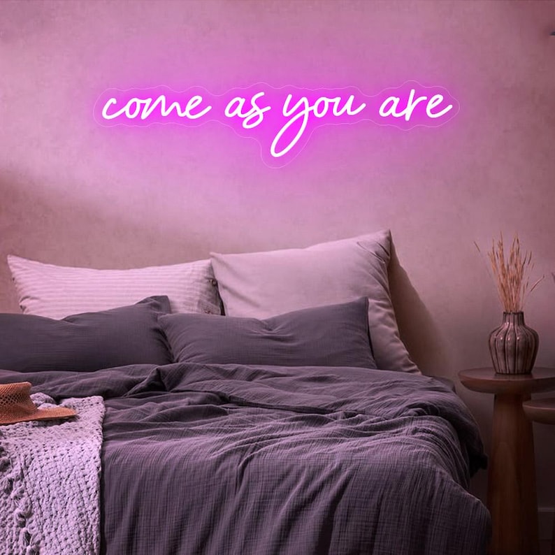 Come As You Are" LED Neon sign by by LedNeons.com - creating a fun and inspiring atmosphere. - glowing warmly on a wall.