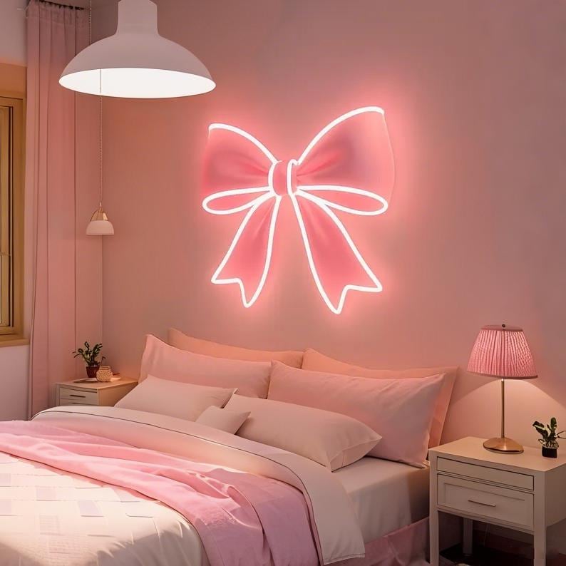 Pink bow-shaped LED Neon sign by LEDNeons - glowing softly on a wall, adding a cute and feminine touch to the decor.